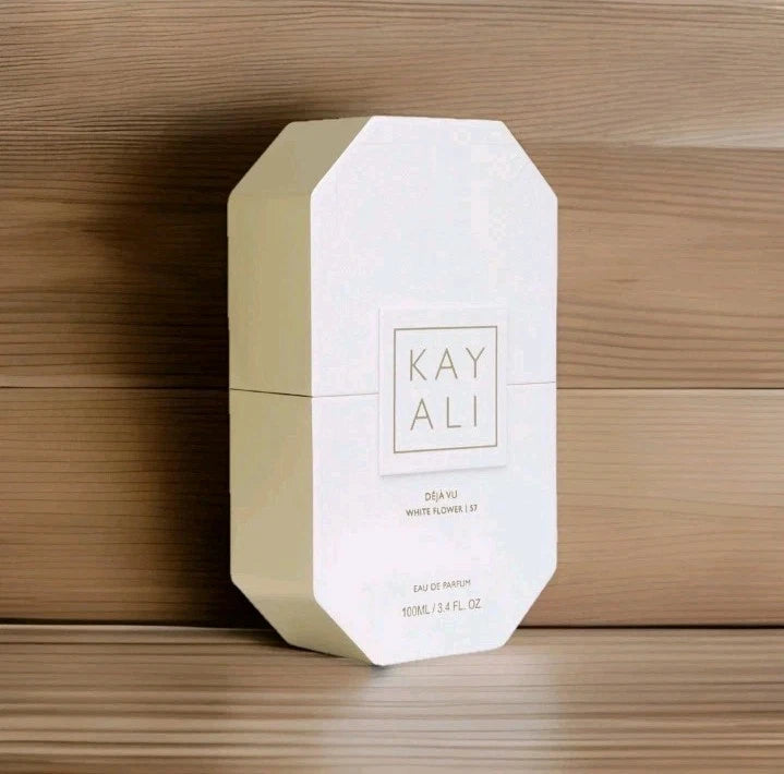 A white octagonal box of Kay Ali Sea Yu White Flower Lip Eau de Parfum, standing upright on a light wood surface against a darker wood background.