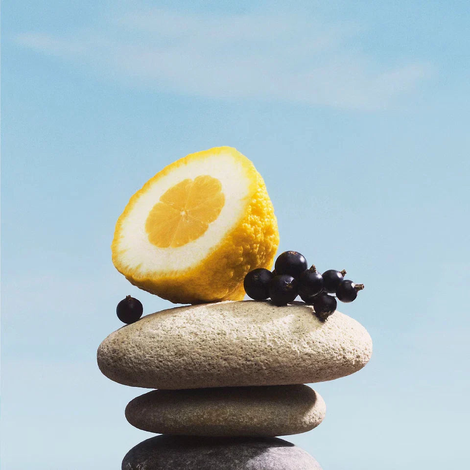 Half a lemon and blackberries on stacked stones with a clear blue sky background