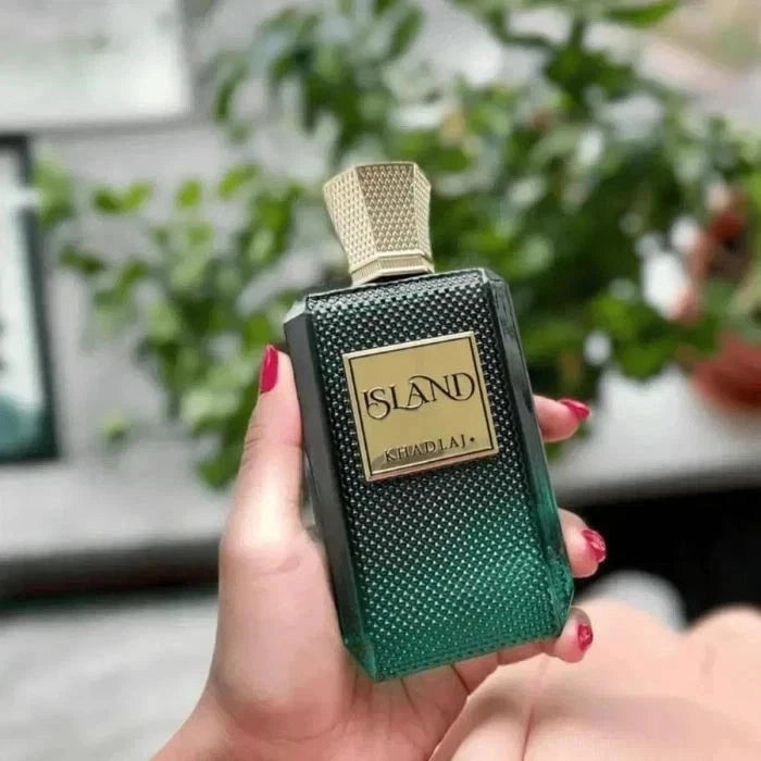 Hand holding a green and gold 'ISLAND' perfume bottle with blurred greenery in the background