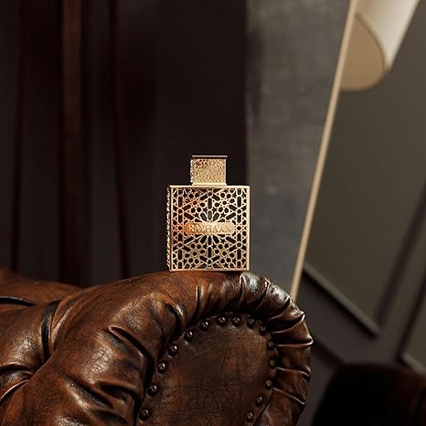 Perfume bottle with intricate design held by a hand on a leather surface