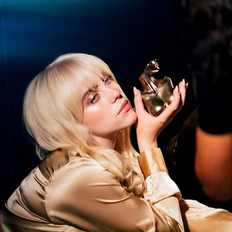 Person with blonde hair holding a small sculpture against a dark background