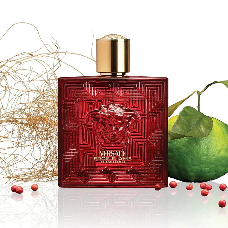 Red Versace perfume bottle with gold cap, green fruit, and decorative elements on a white background