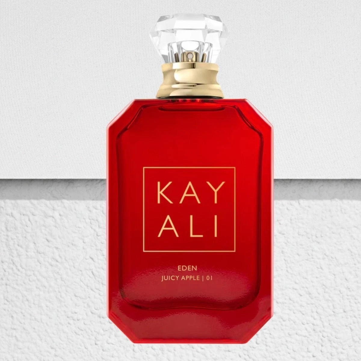 Red perfume bottle with gold cap on a textured white background