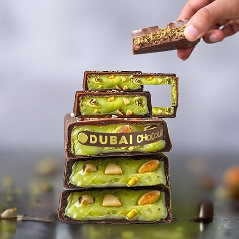 Stack of chocolate bars with green filling and 'Dubai Choco' branding, held by a hand against a blurred background.
