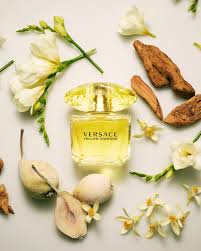 Versace perfume bottle surrounded by flowers and pears on a light background